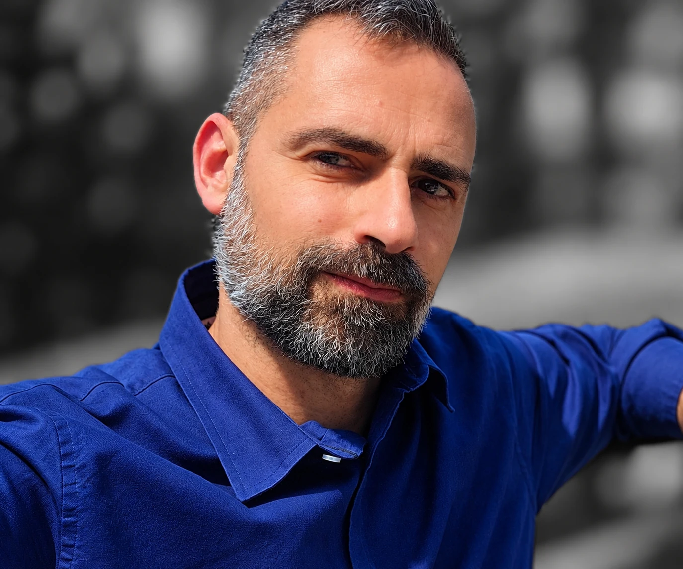 Ritratto di Mirko Labinero con camicia blu indaco e sfondo sfocato in bianco e nero